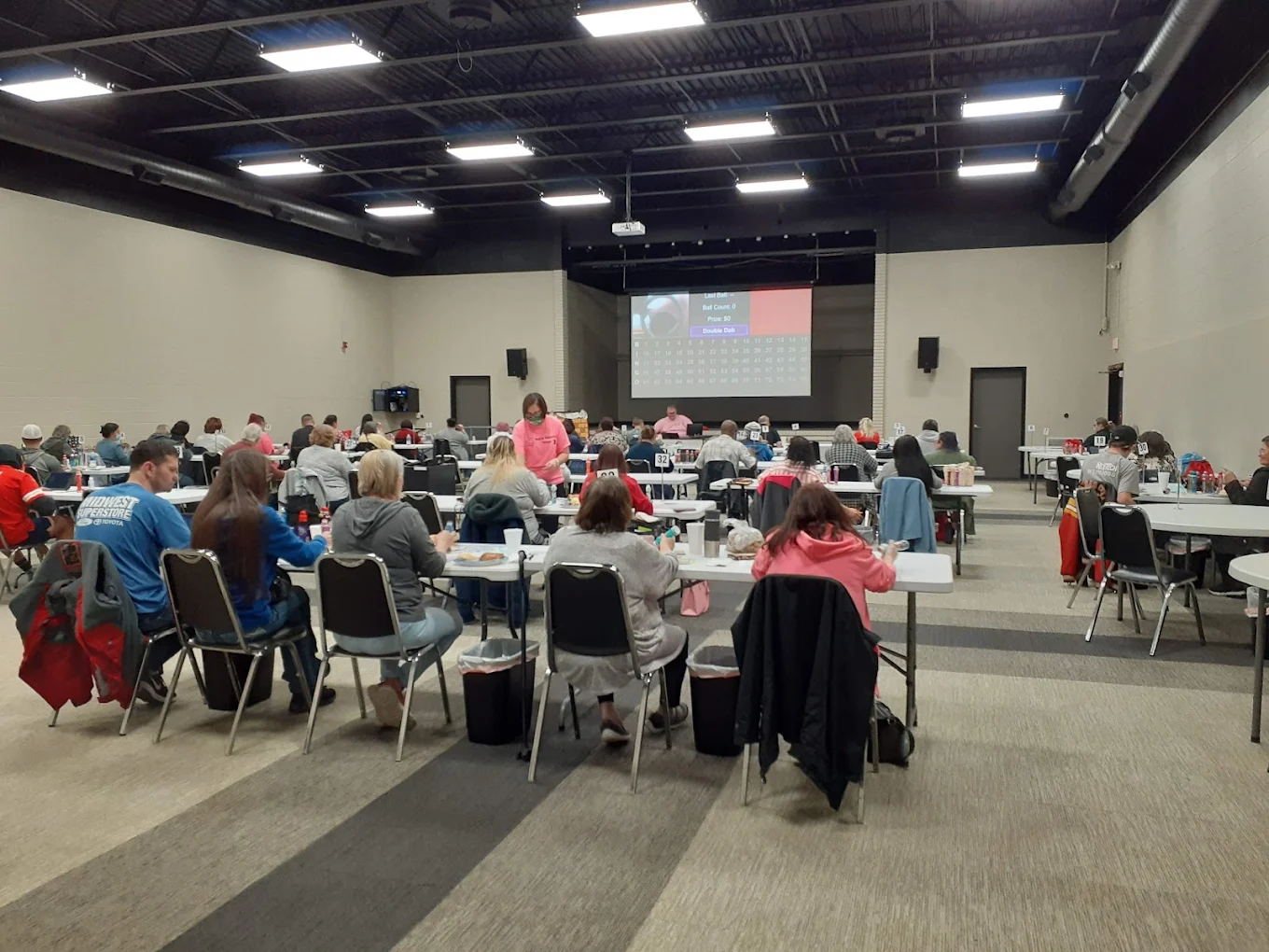 Guests seated at long tables facing the drop-down screen at SandHills Event Center